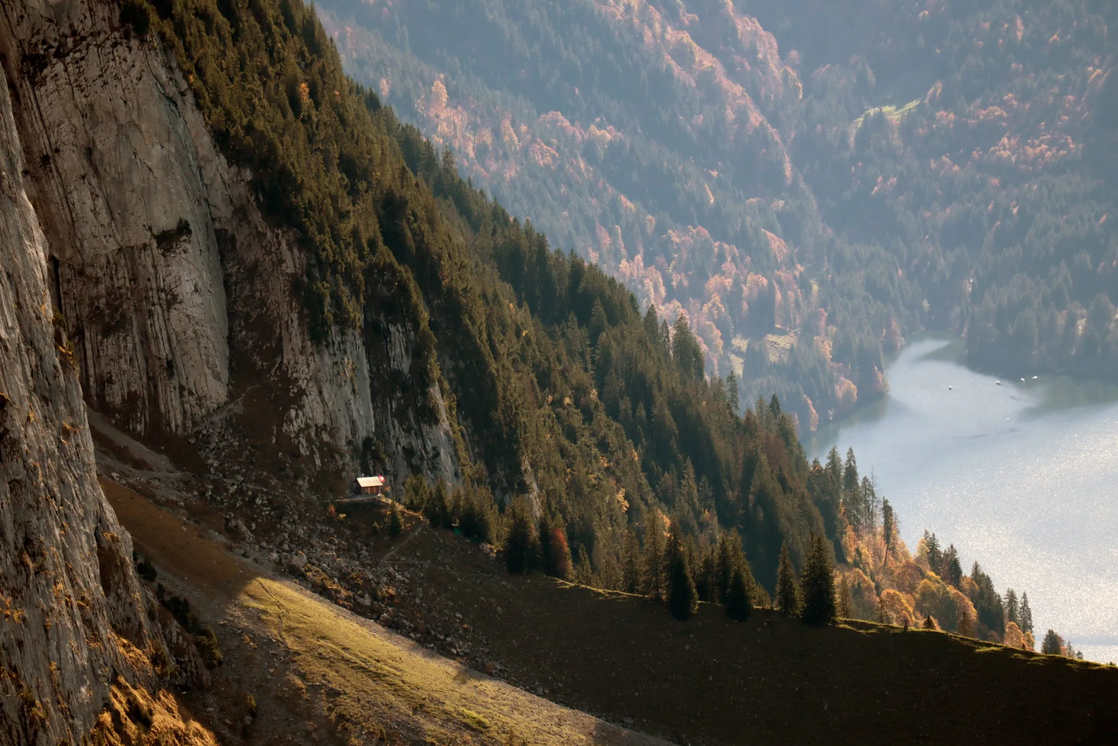 Steep drop from a cliff face down to Lake Wägital framed by autumn forest.