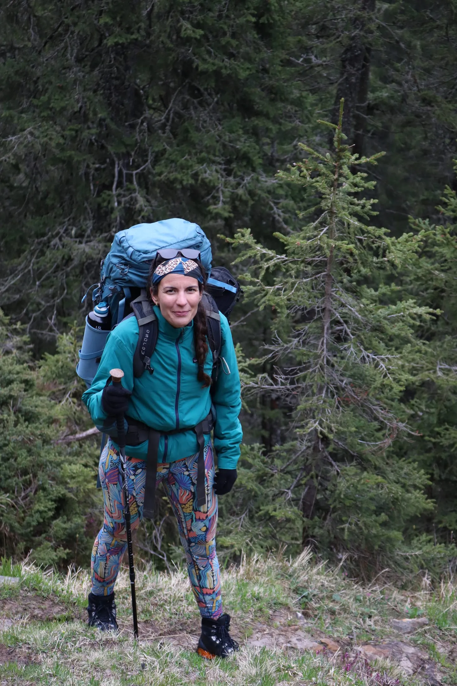 Hiker in a teal jacket and colorful leggings posing on the forested trail.