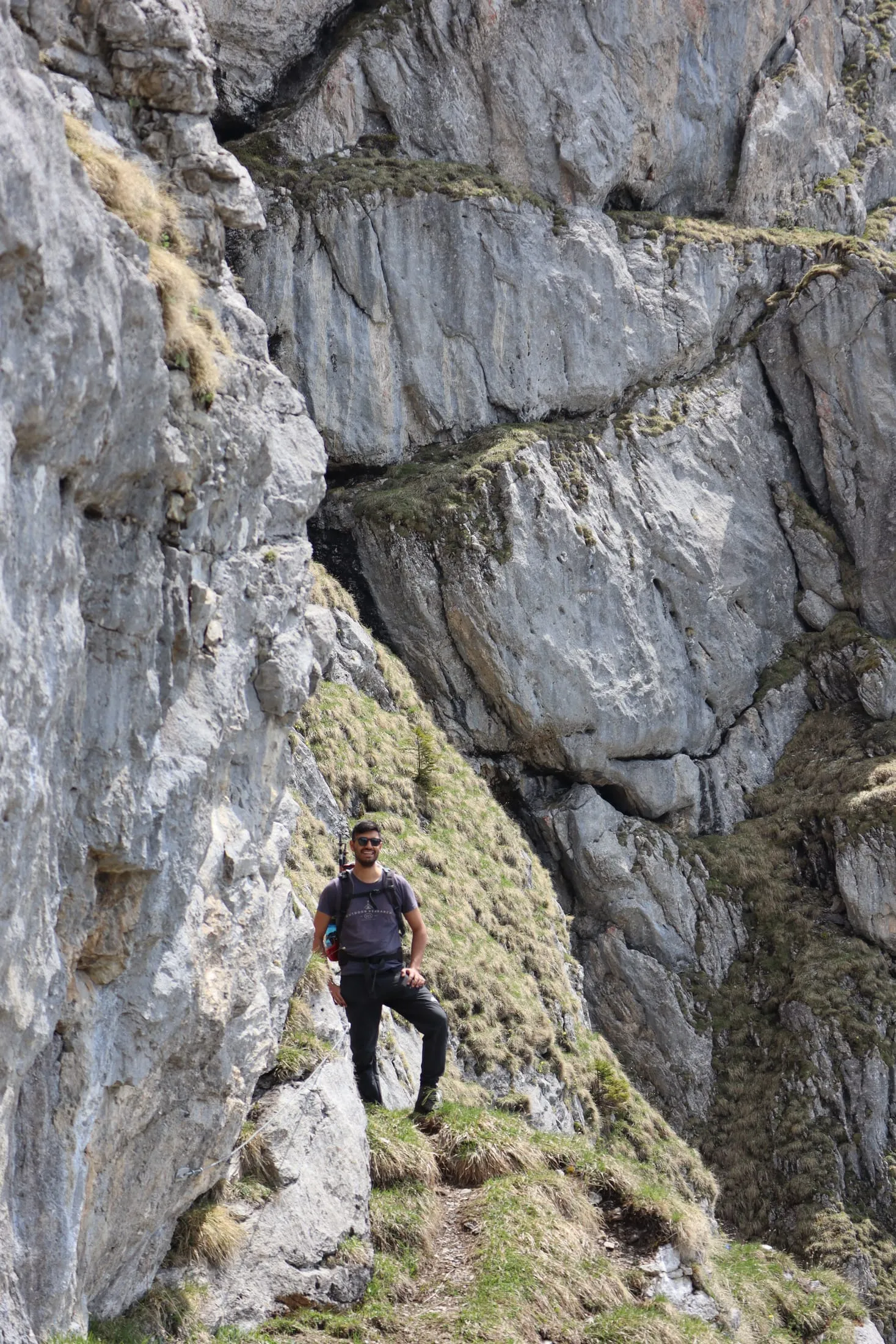Hiker traversing a cracked limestone slab with tufts of grass clinging to the rock.