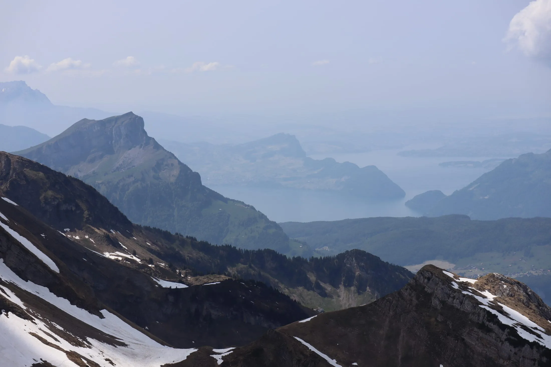 Hazy view down to Lake Lucerne with snow patches in the foreground ridges.