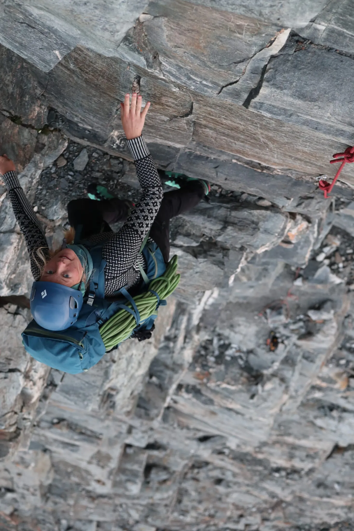 Climber with helmet and rope working up a steep rock face.