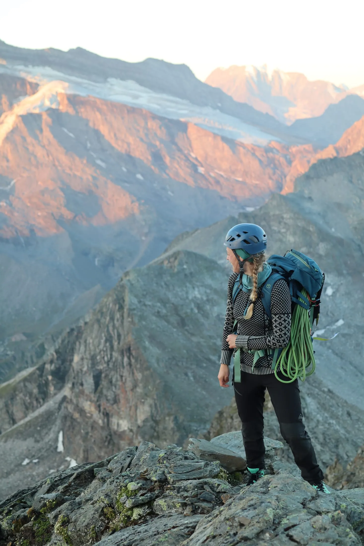 Climber on the ridge with a coil of rope and morning light on distant peaks.