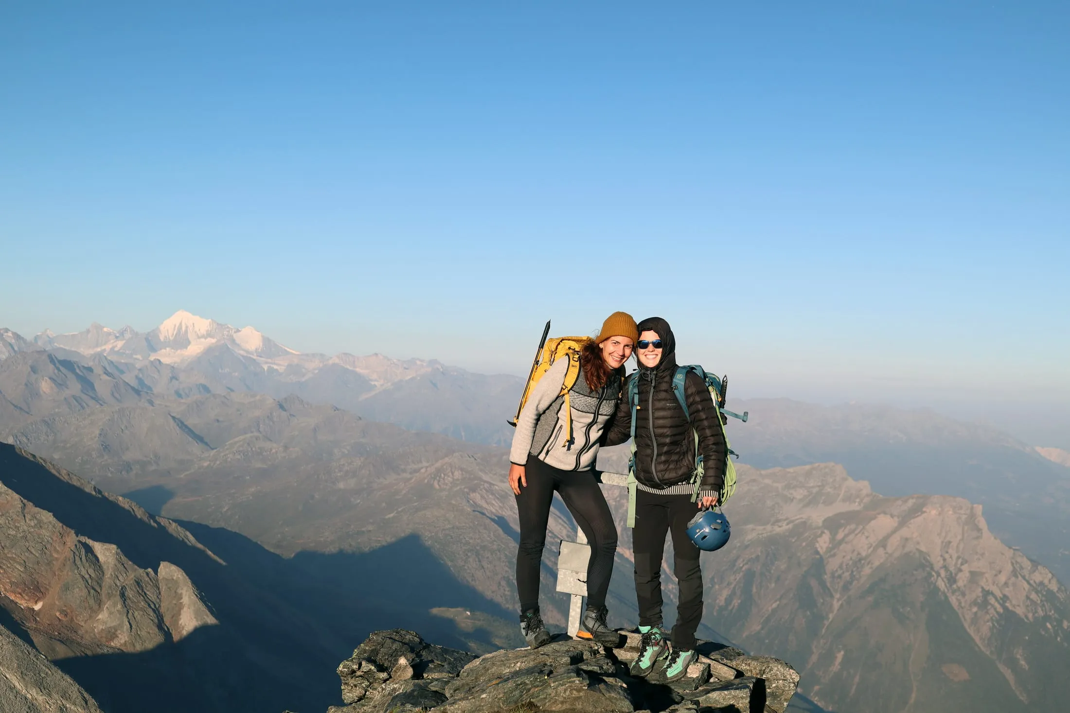 Two hikers on the Bortelhorn summit with the Weisshorn group behind.