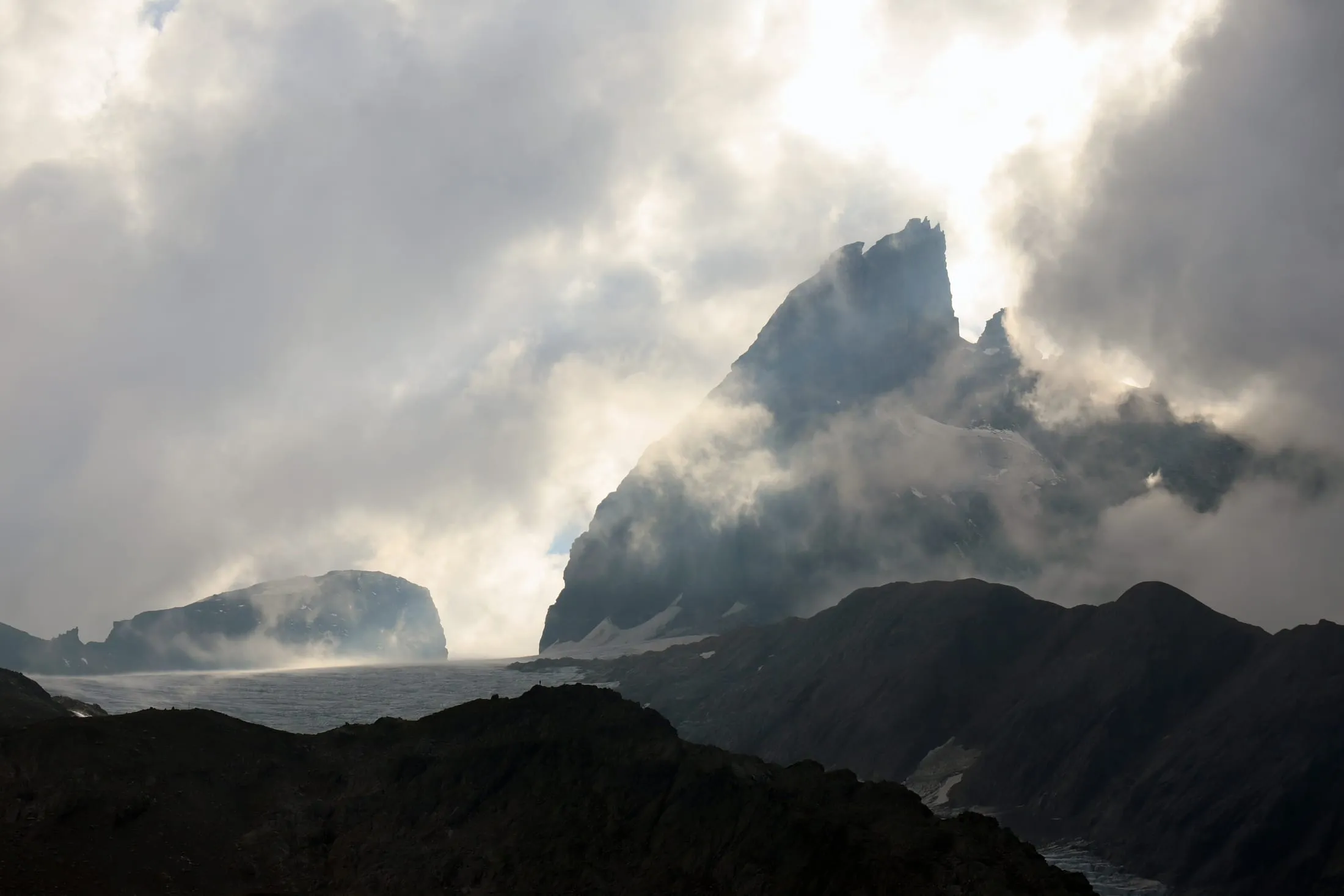 Dramatic rock spire between backlit clouds above the glacier.
