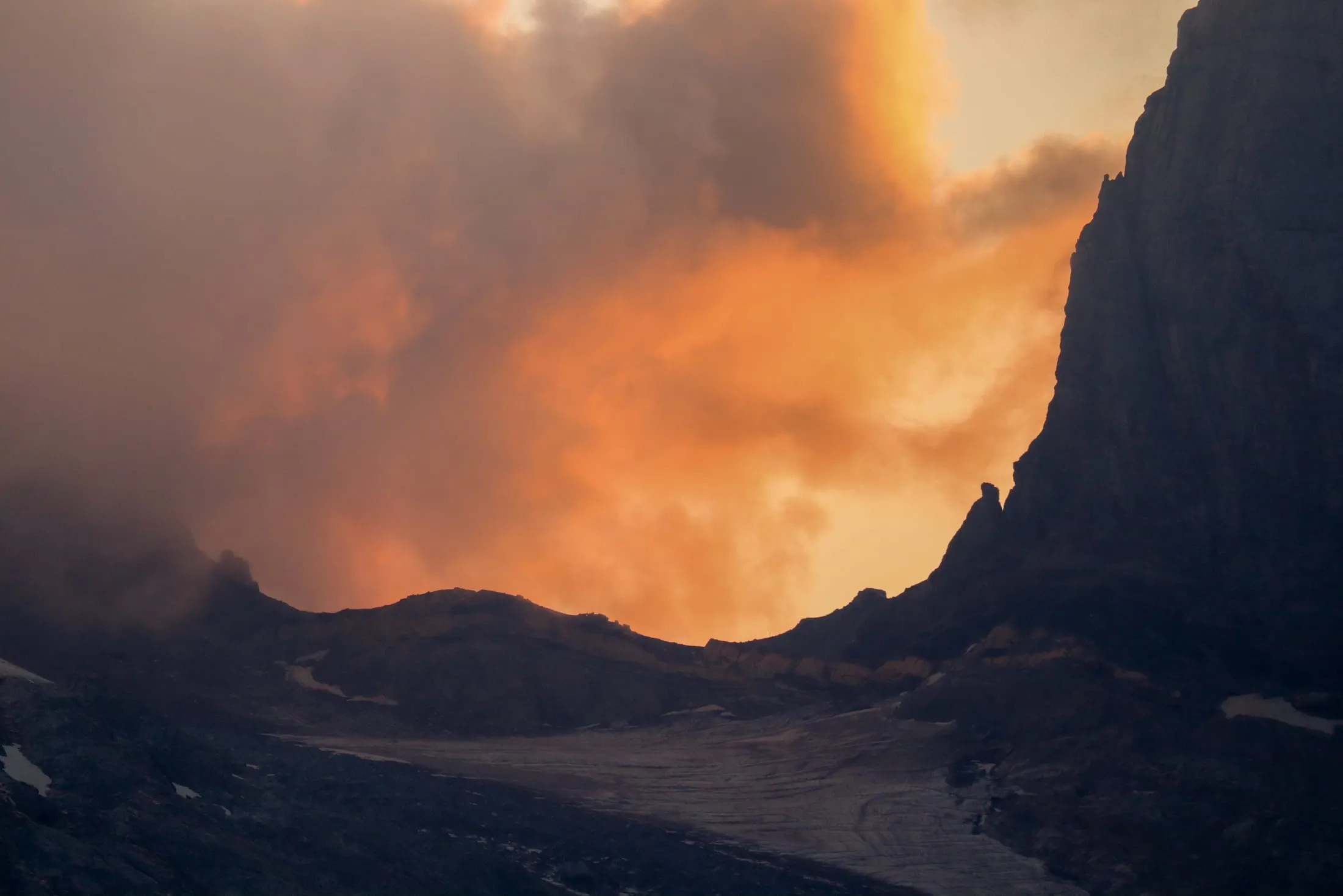 Glowing orange alpenglow over the glacier with a silhouetted rock spire.