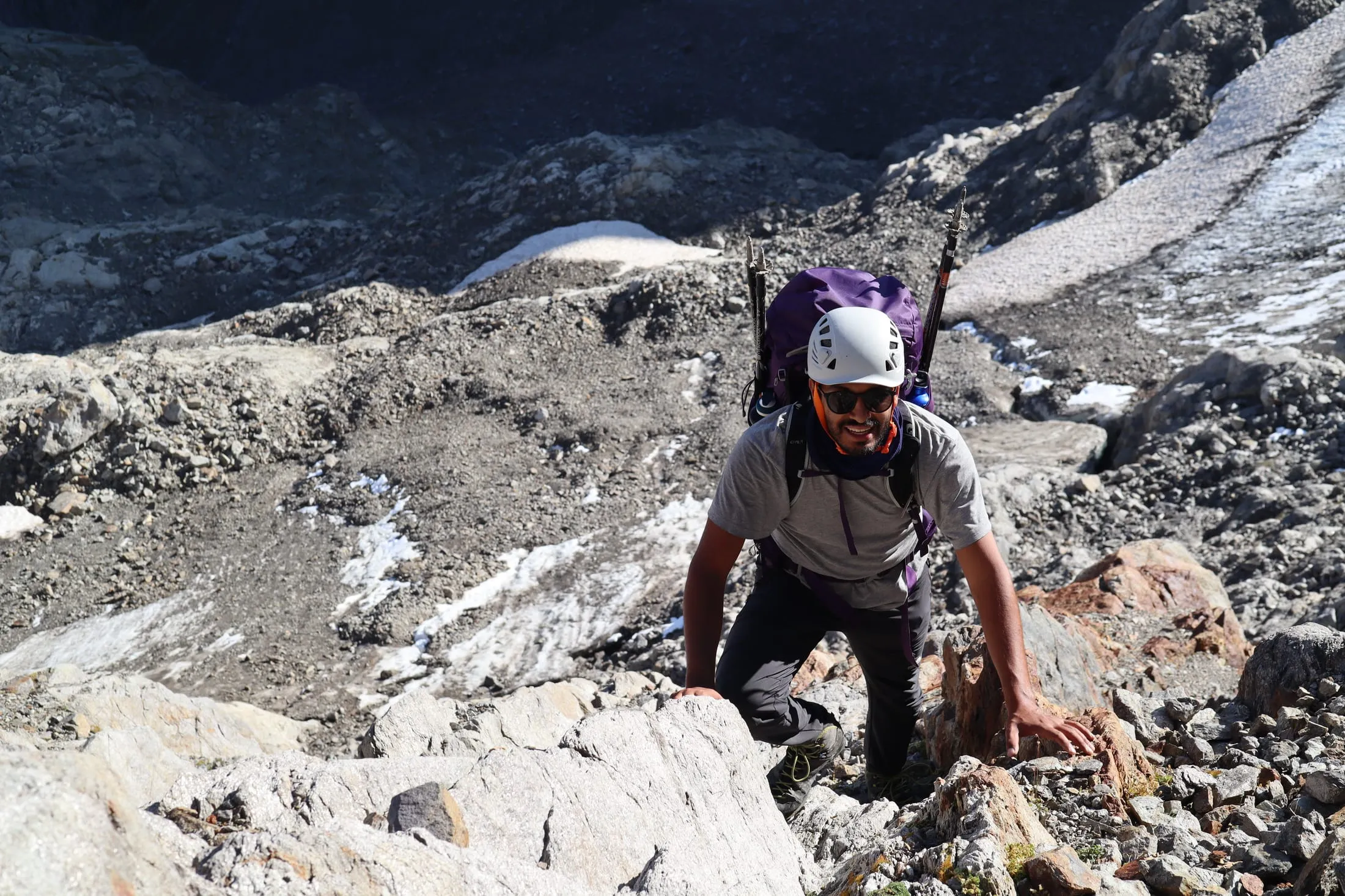 Mountaineer with helmet and ice axe carefully descending a snowy slope.
