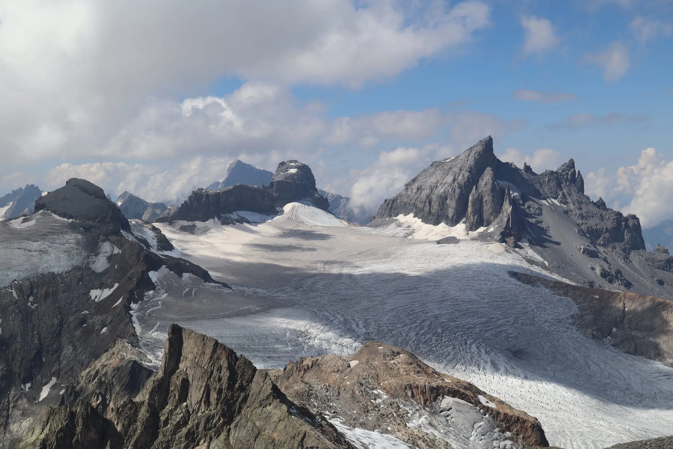 Wide panorama over the glacier with jagged peaks and drifting clouds.