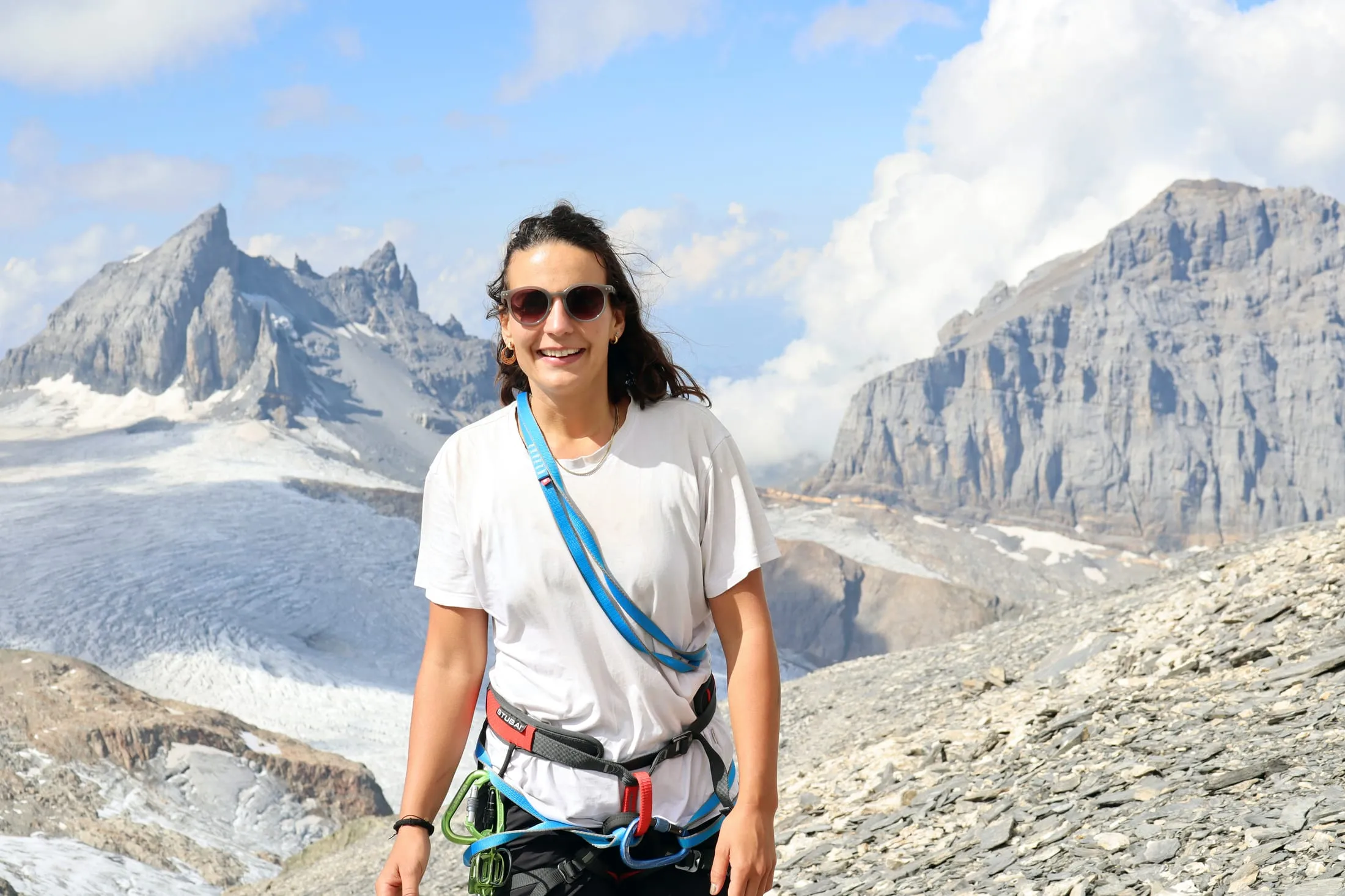 Smiling climber in a harness with the glacier and rocky peaks behind her.