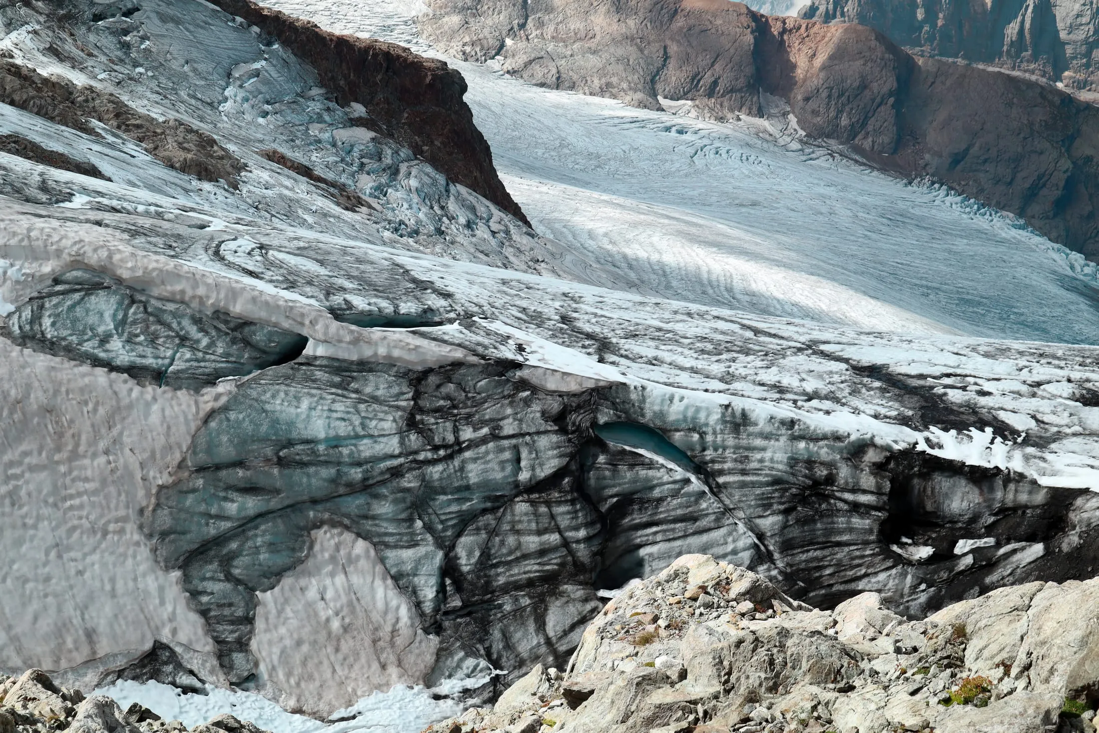 Close-up of a crevasse with turquoise meltwater between dirty ice ridges.
