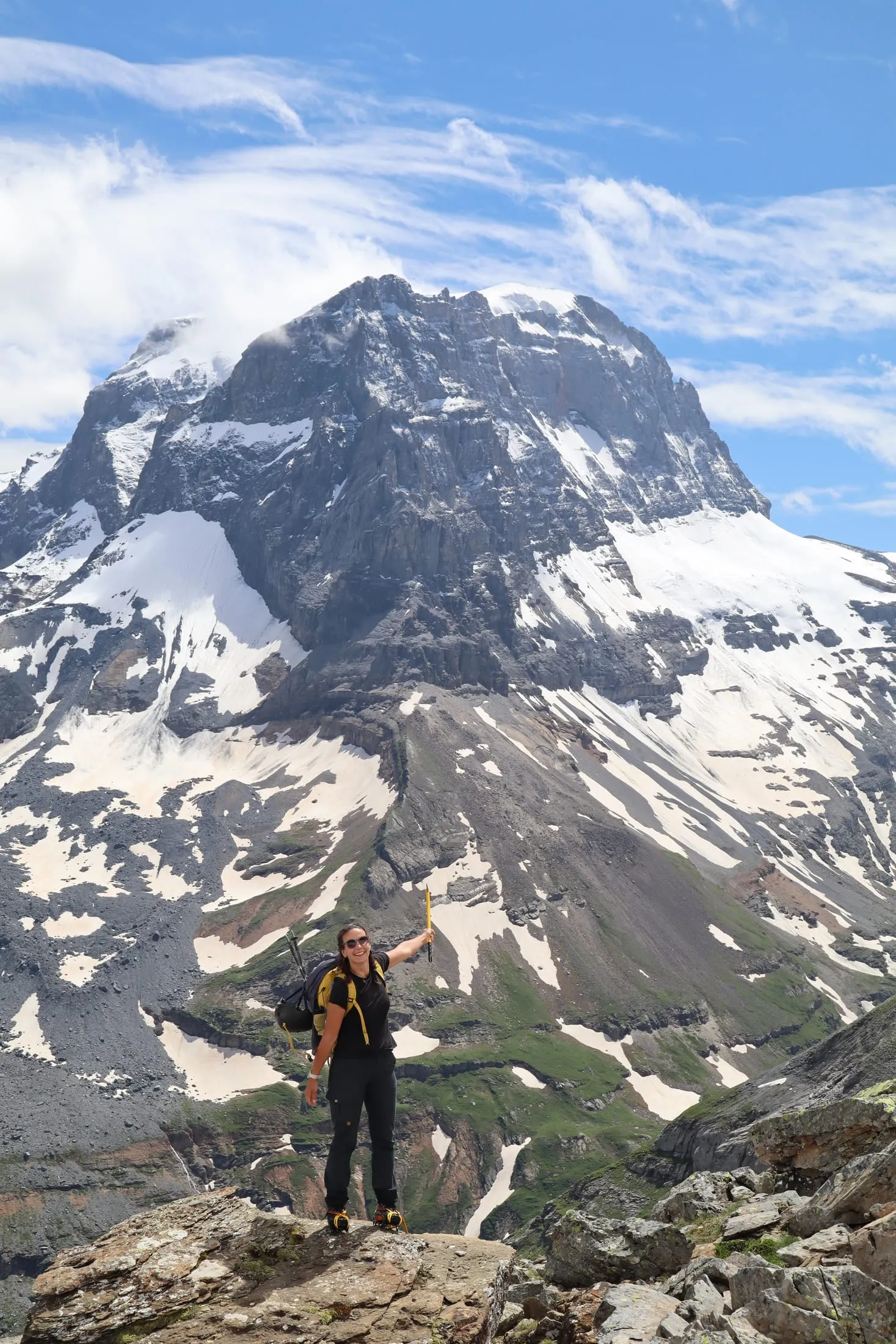 A mountaineer with an ice axe climbs a snow slope, a large glaciated mountain flank behind.