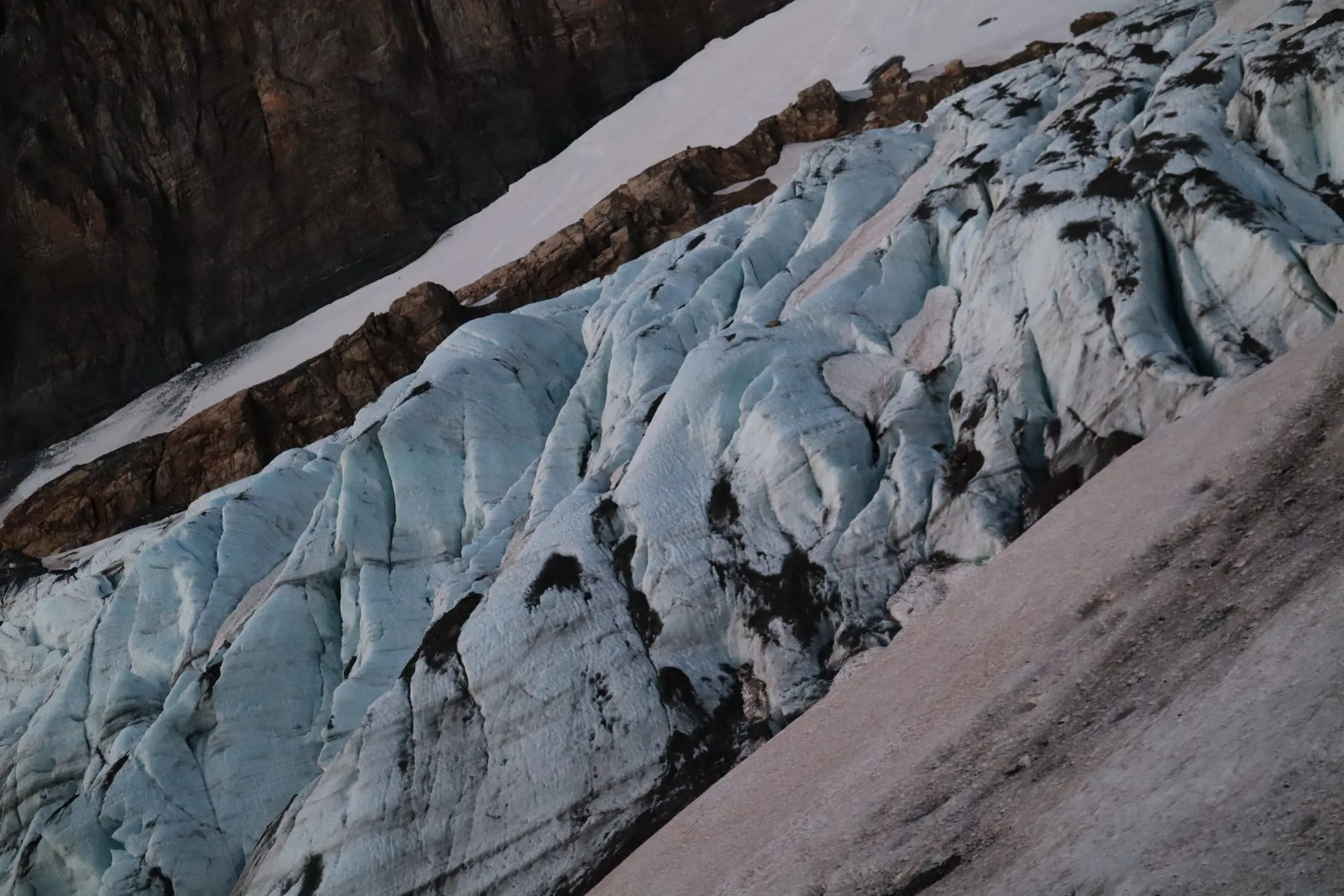 Close-up of a blue glacier wall riddled with crevasses, framed by snow and dark rock.