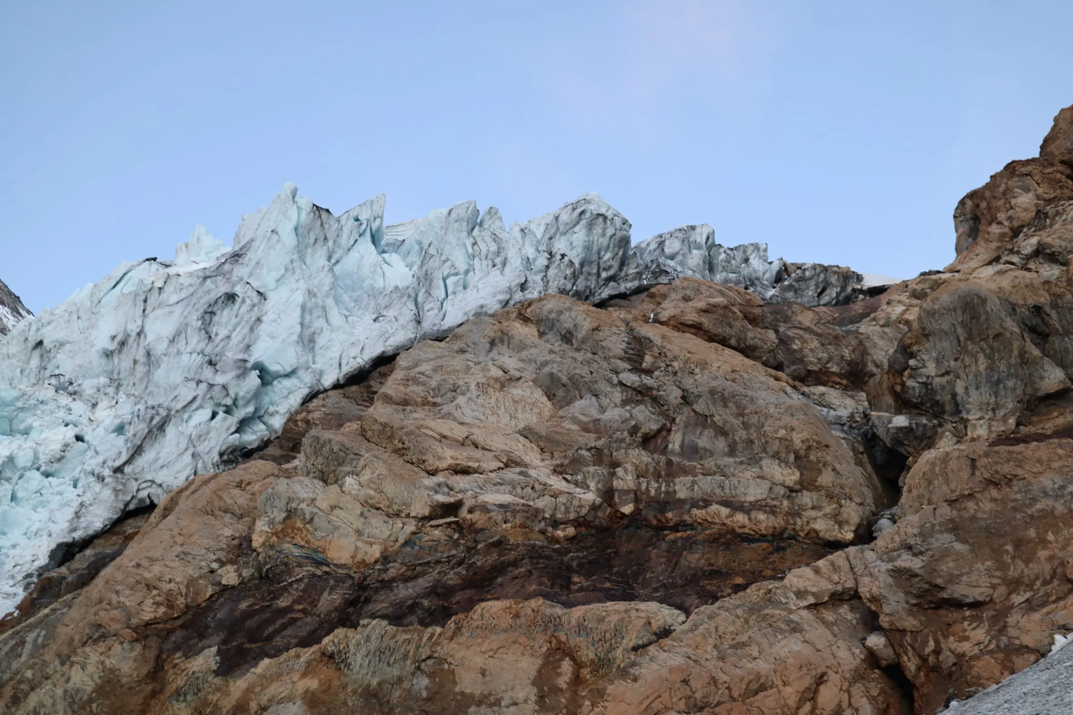 Broken seracs along the top of a massive brown rock face in blue twilight.
