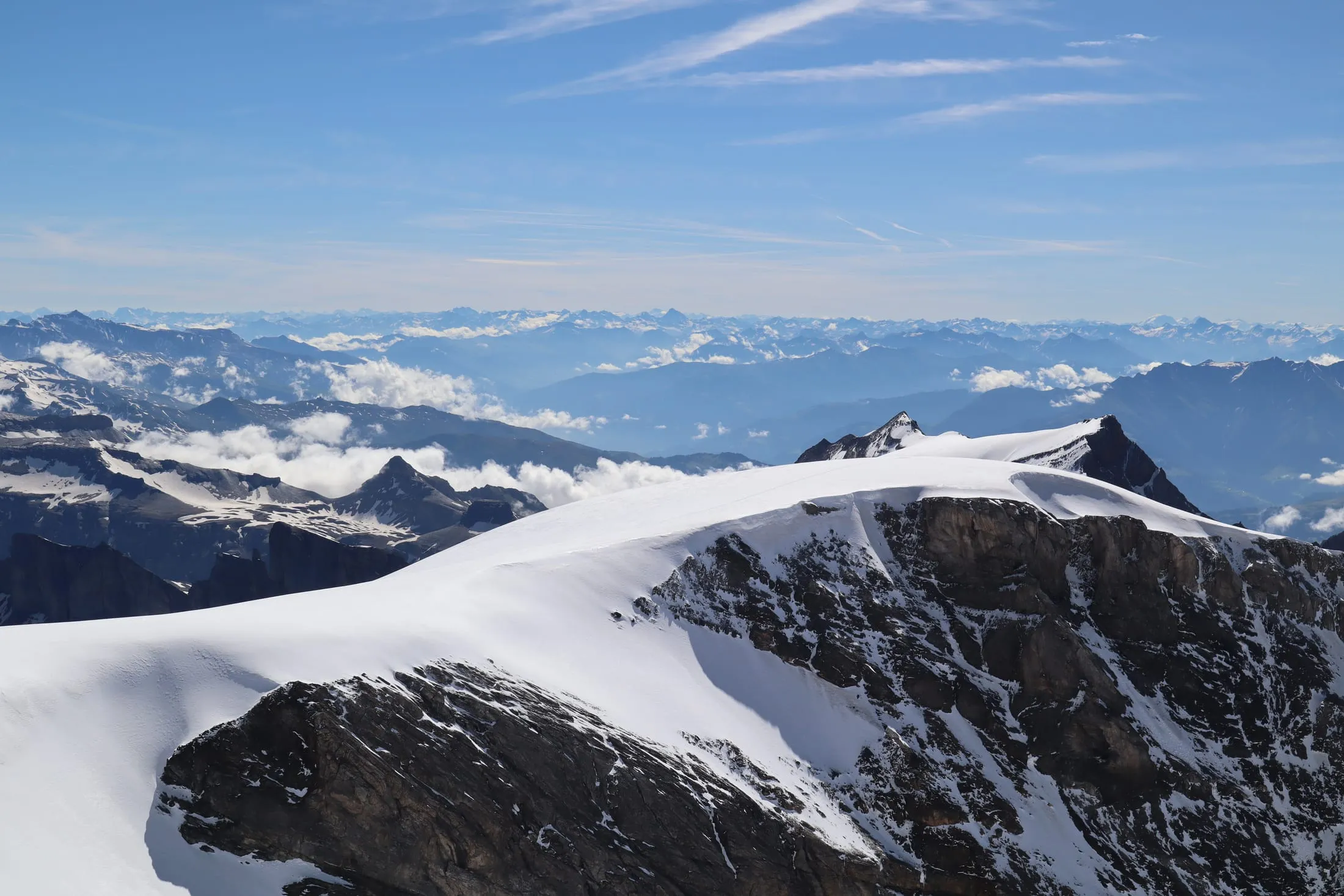 Summit panorama with a broad snow dome and endless mountain ranges to the horizon.
