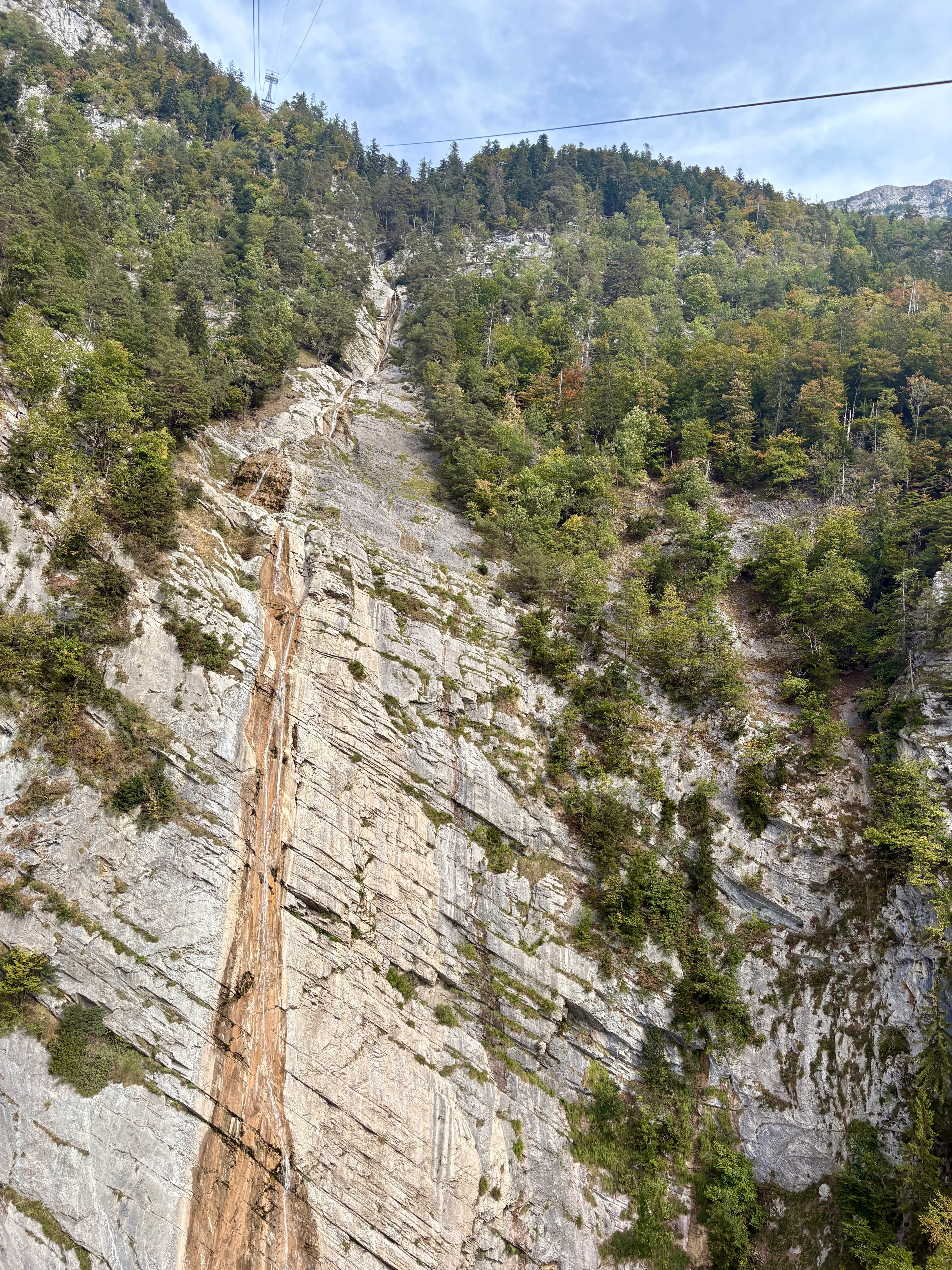 The view from the Palfries cable car down a steep, layered limestone face with a water-worn gully cut into the rock.