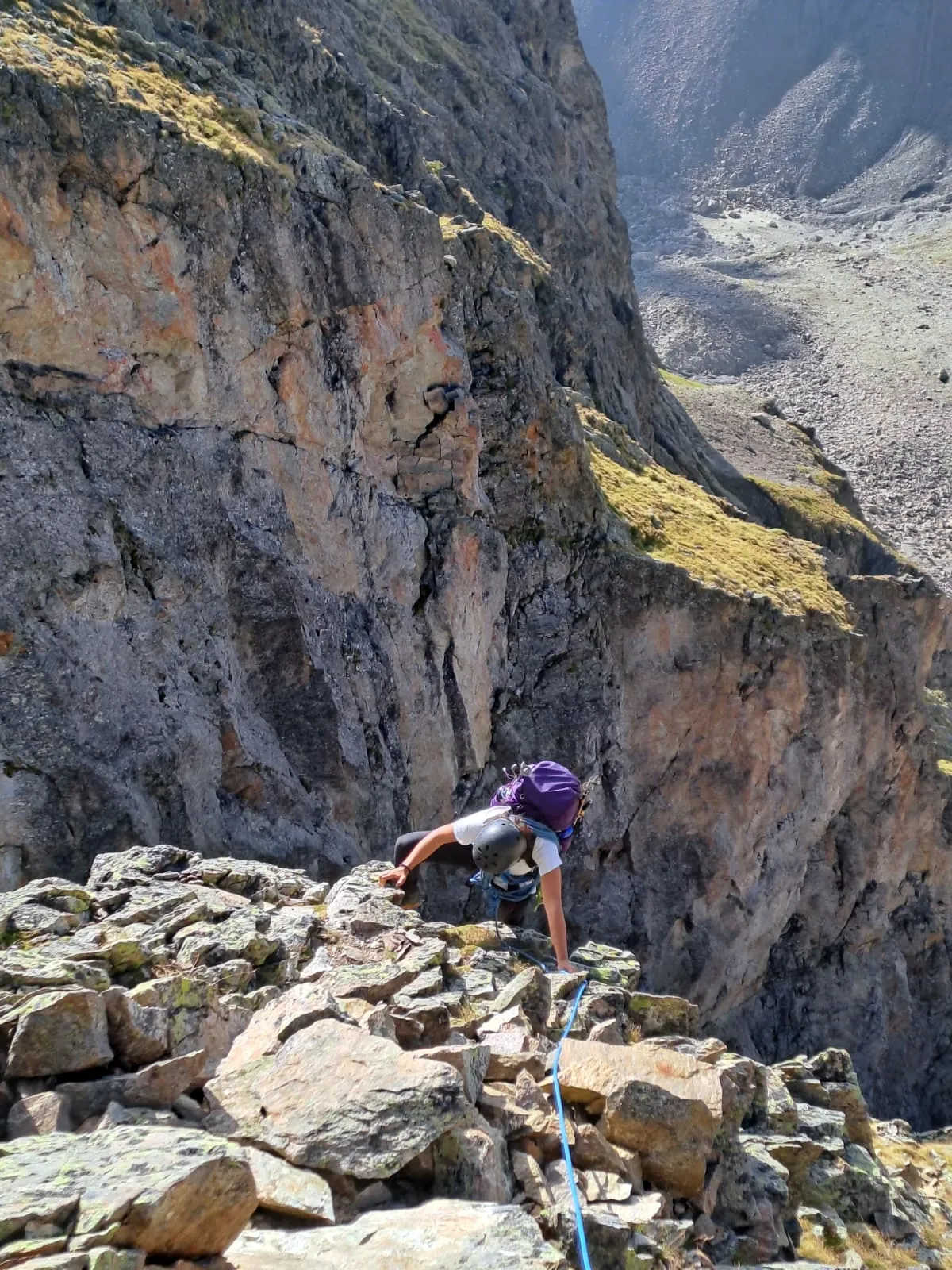 Climber on a rope working up a steep rock face with a backpack.