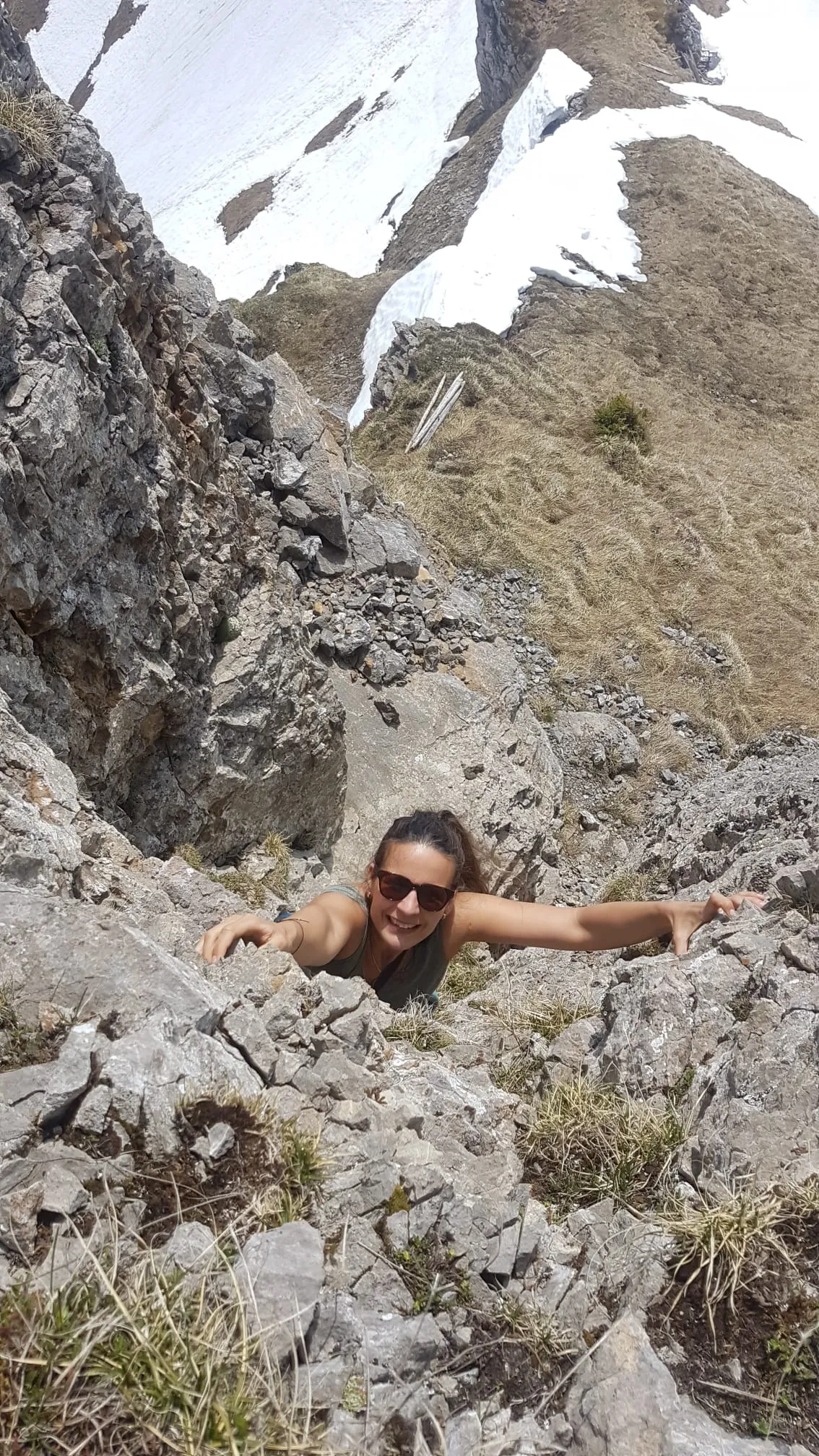 Scrambling up a steep rocky gully, smiling at the camera with snow patches above.
