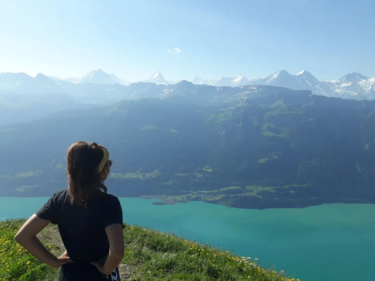 Una senderista de pie sobre la cresta herbosa contempla el turquesa lago de Brienz y, al fondo, los nevados Alpes berneses.