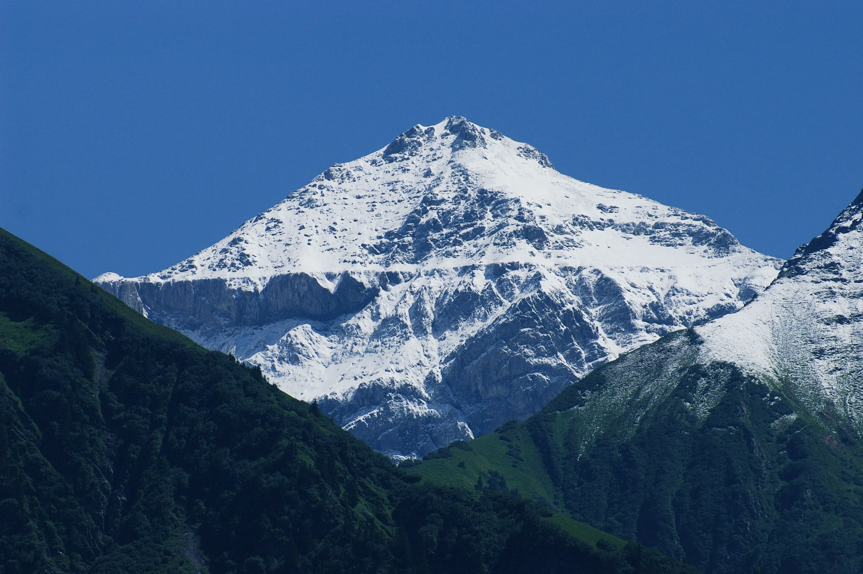 The Hausstock (3158 m) in the Glarus Alps, freshly dusted with snow above green pastures.