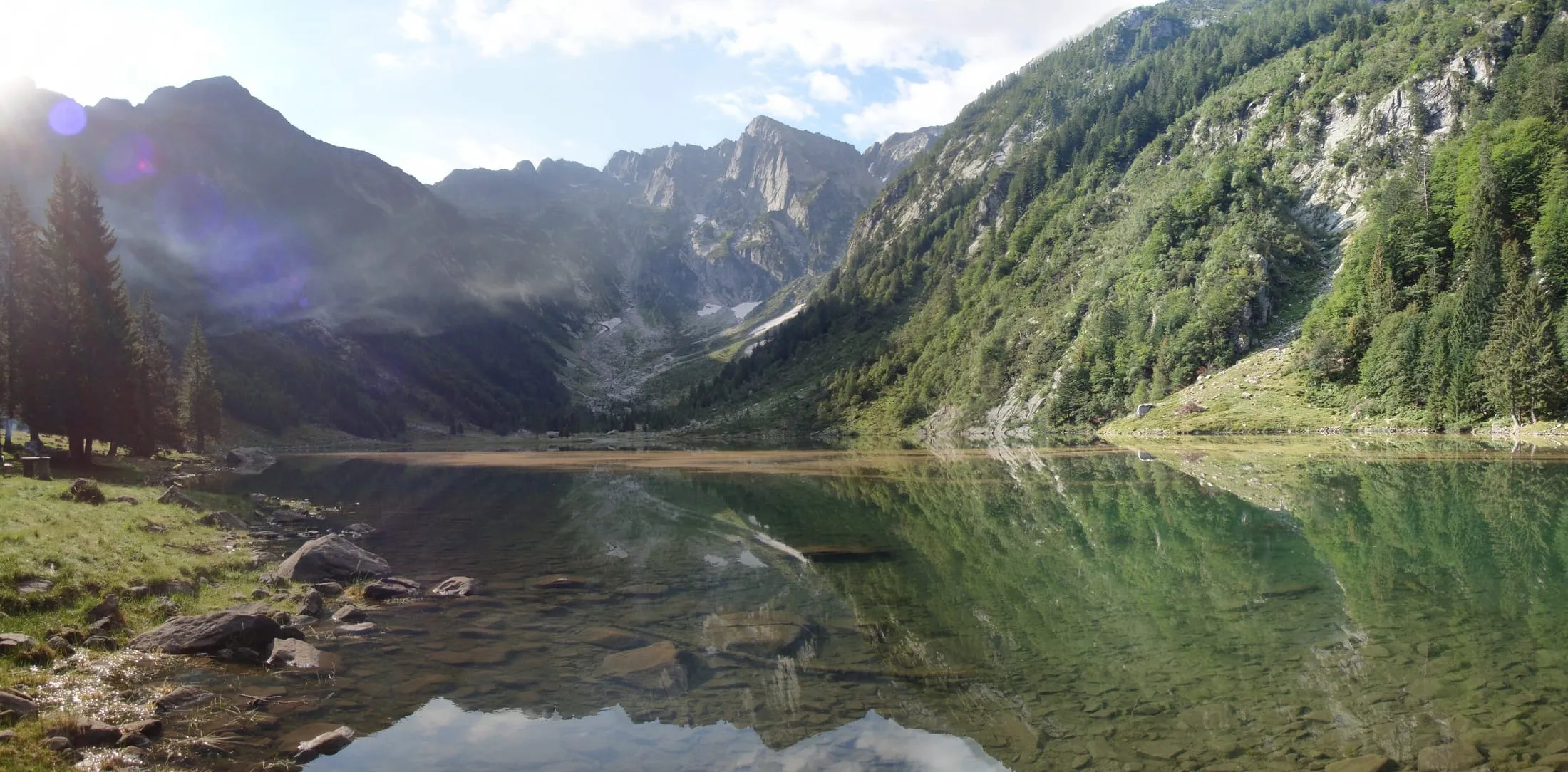Early morning at Lagh de Cama, with mountains reflected in the still water.