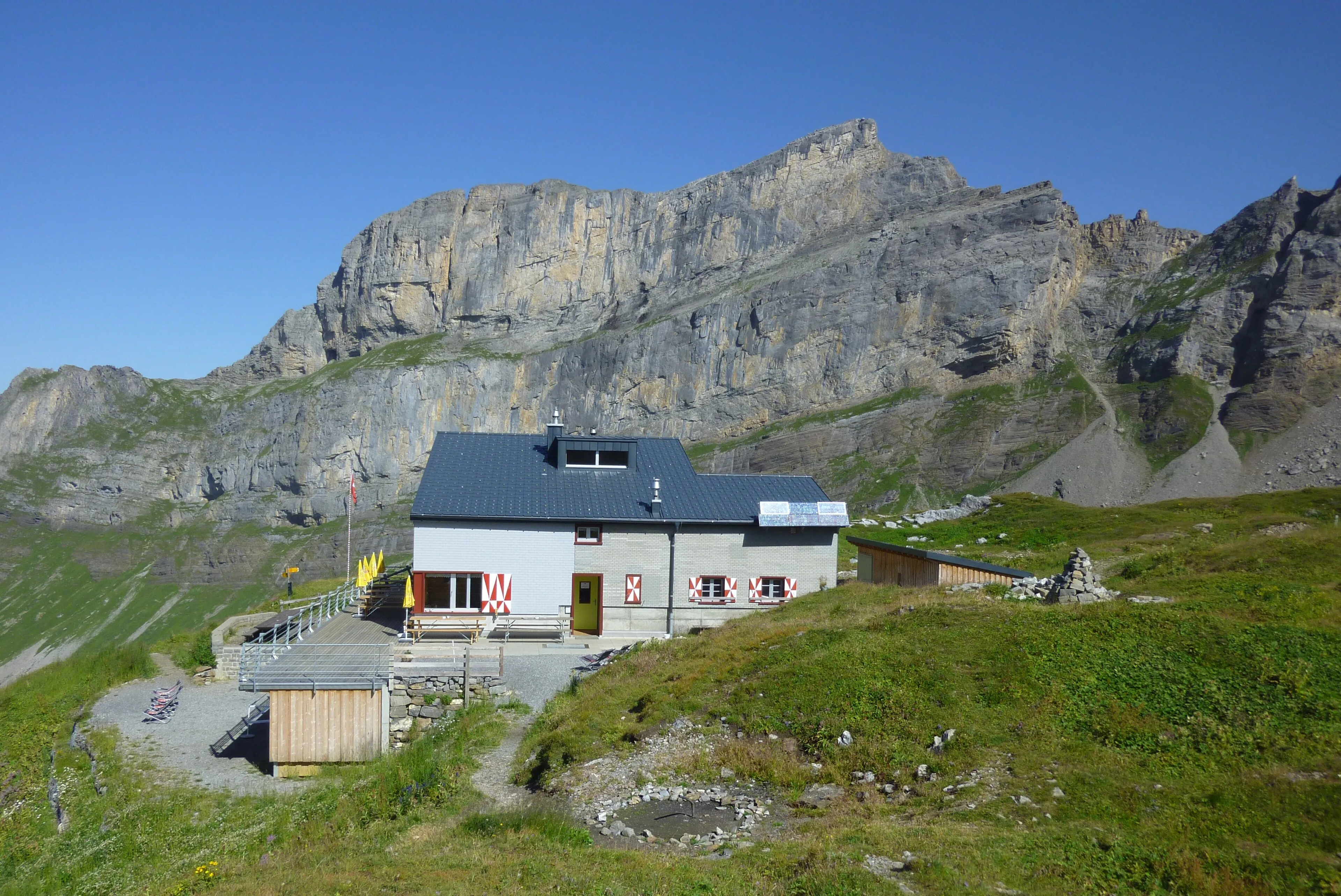 The Rugghubel hut above Engelberg, beneath a mighty rock wall on a clear summer day.