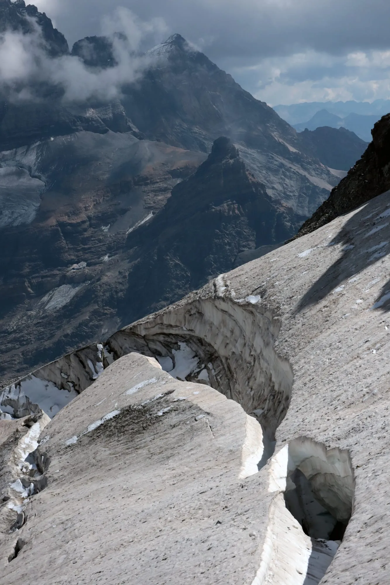 Open crevasses and icefalls on the glacier slope, neighbouring peaks hazy under cloud behind.