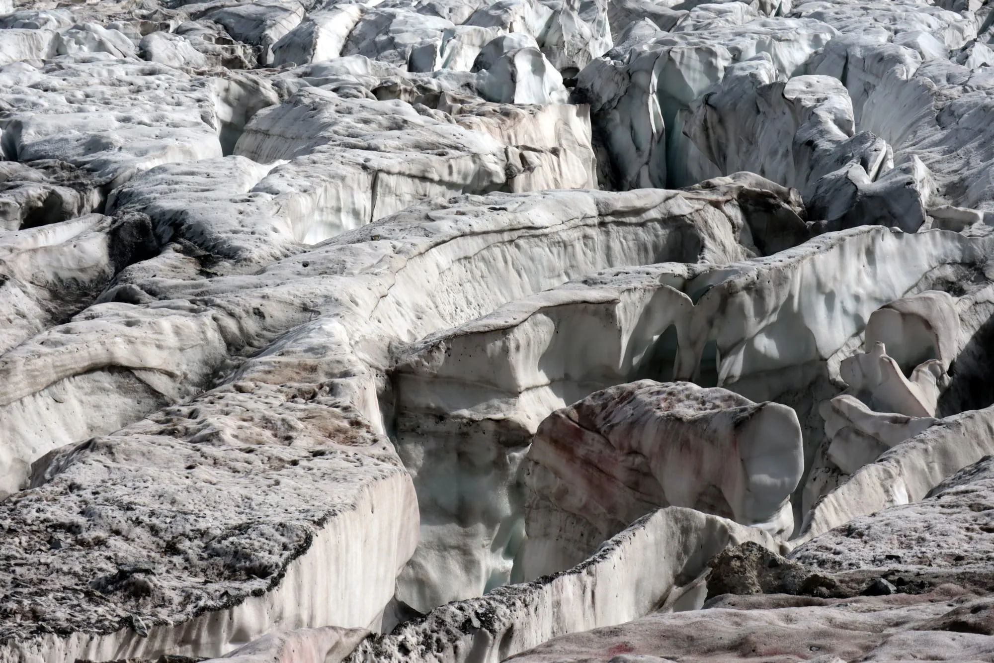 Close-up of a maze of crevasses: layered ice walls with reddish dust in the bands.