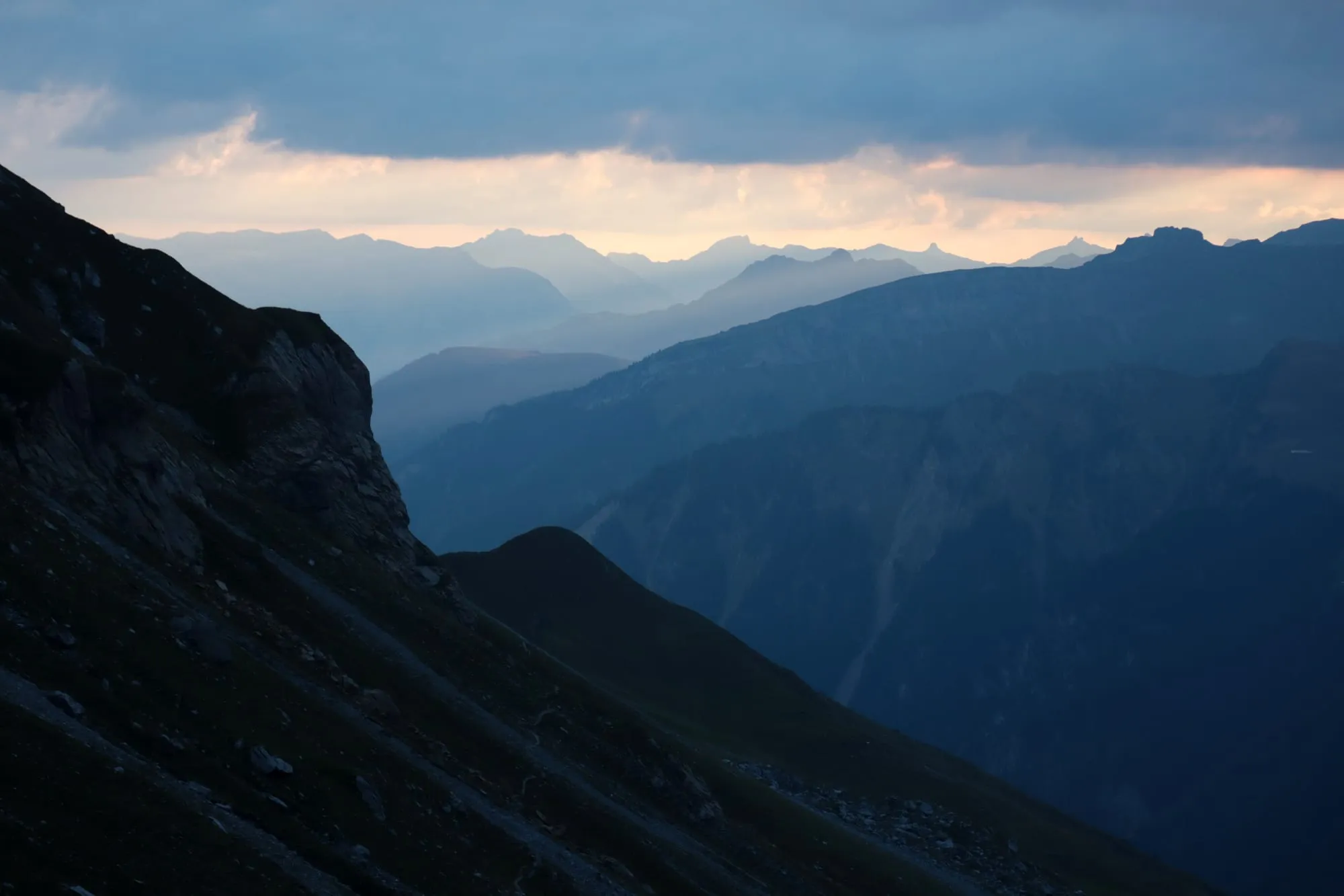 Evening light over layered mountain ranges, a dark rock shoulder in the foreground.