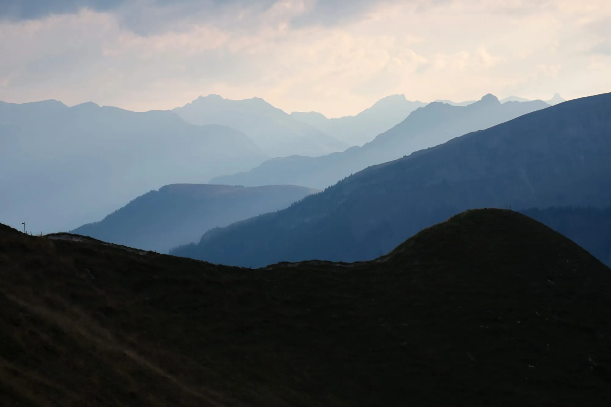 Blue mountain silhouettes in the haze, with the soft grassy backs of the alpine pastures in front.