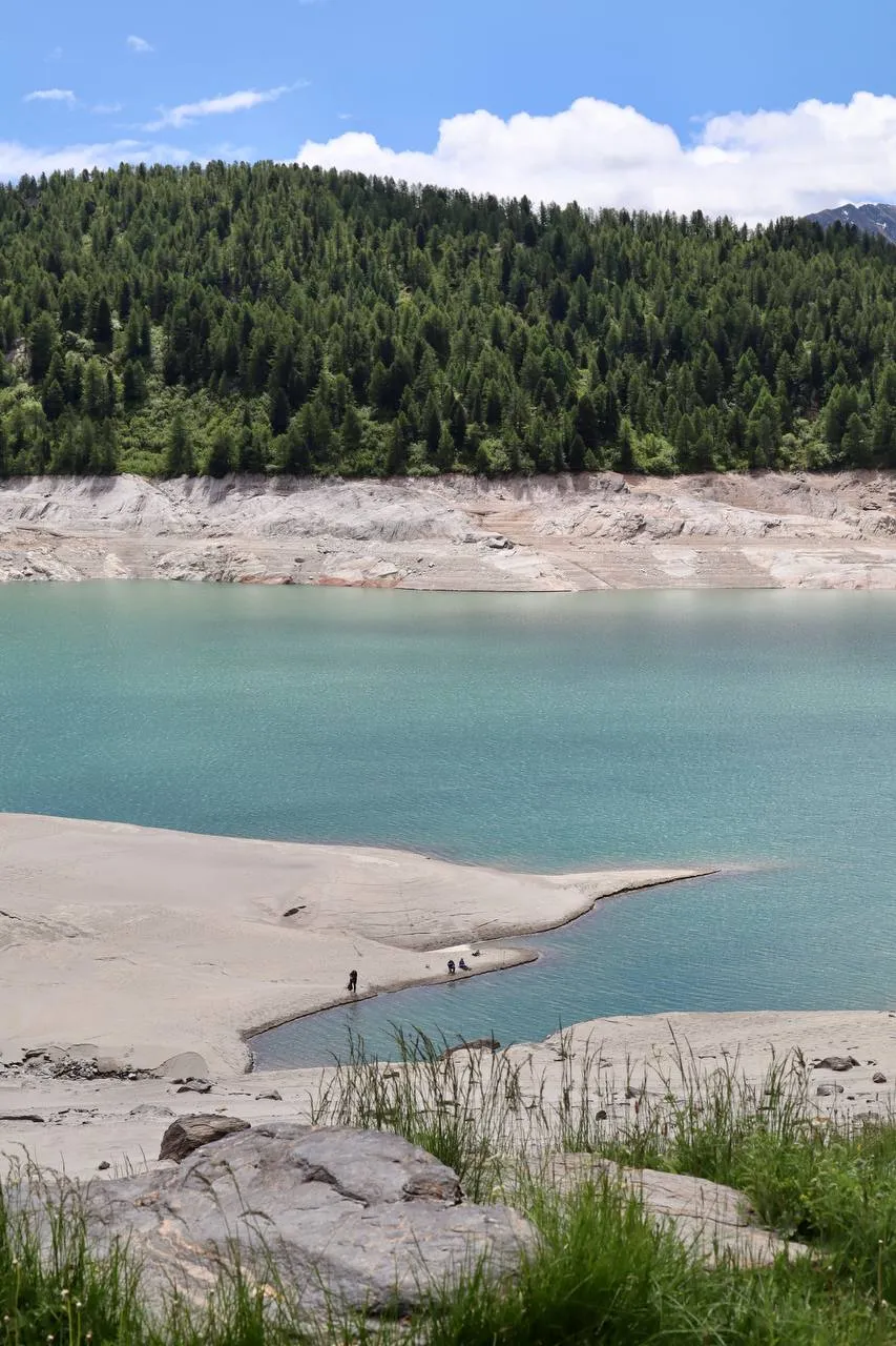 Turquoise Lago Ritom with a pale sandy shore and dark forested slopes above.