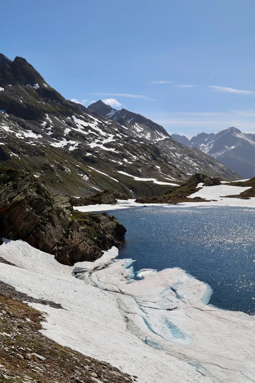 Lago Scuro half-covered in snow and ice floes, ringed by dark, rugged peaks.