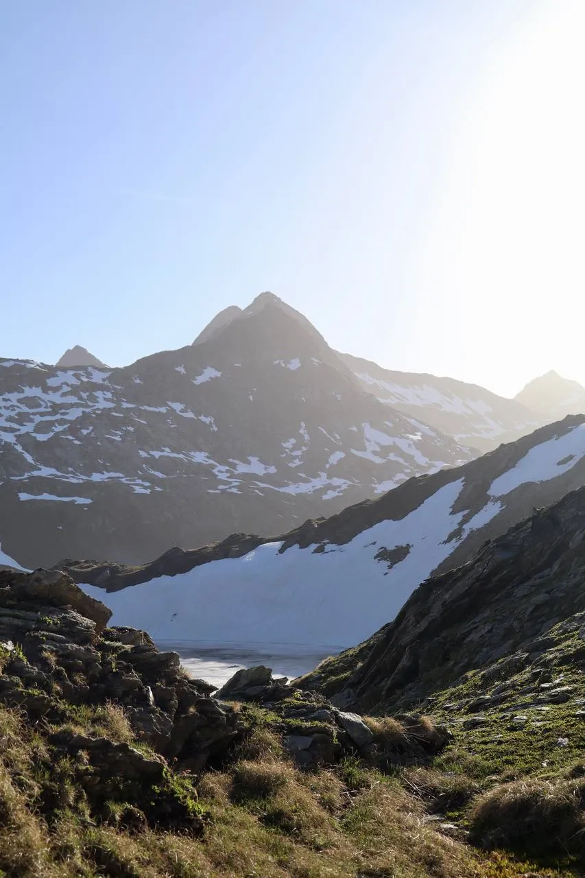 Sharp peak backlit by the morning sun above a wide snowfield.