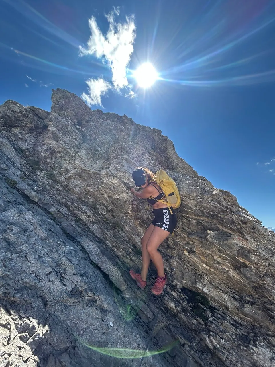 A hiker with a yellow backpack climbs up a sun-lit rock face.