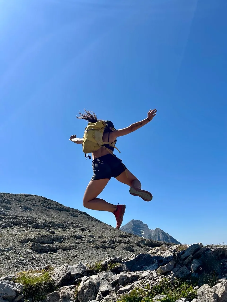 A hiker jumps for joy along a rocky ridge, with snow-capped peaks in the background.