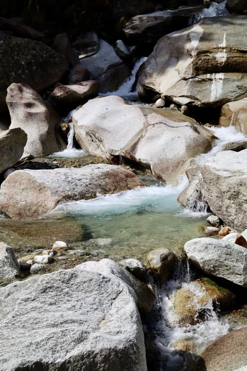 Clear turquoise water flows between smooth white boulders in a mountain stream.