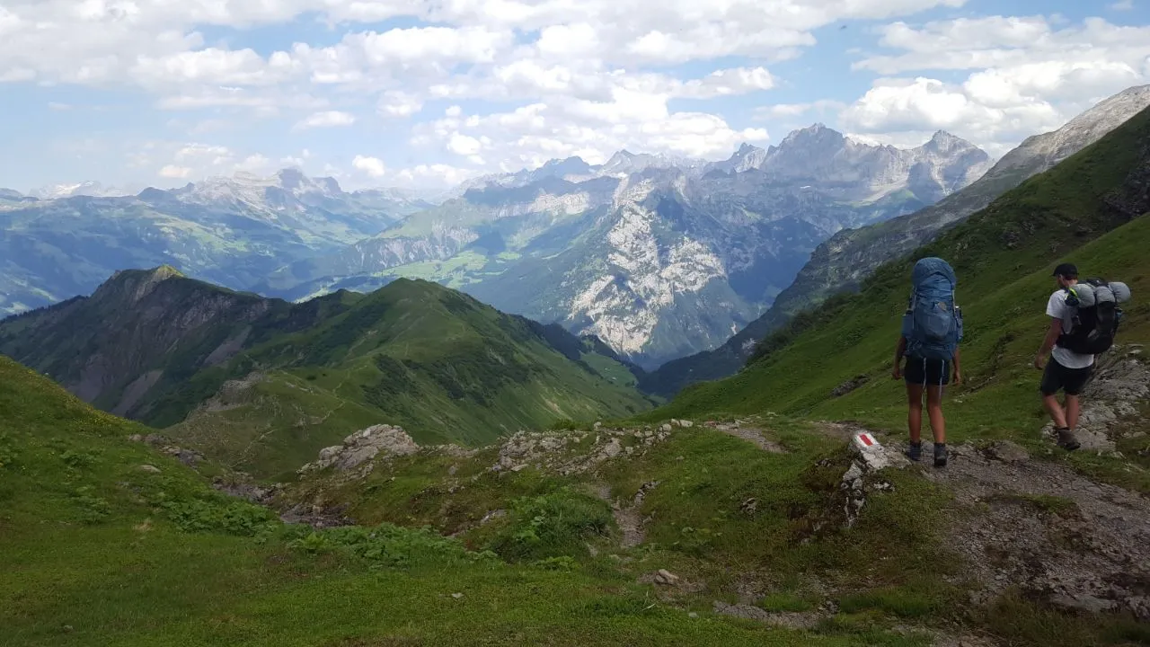 Two hikers at a trail junction with a waymark stone, looking out over layered ridges far down into the valley.