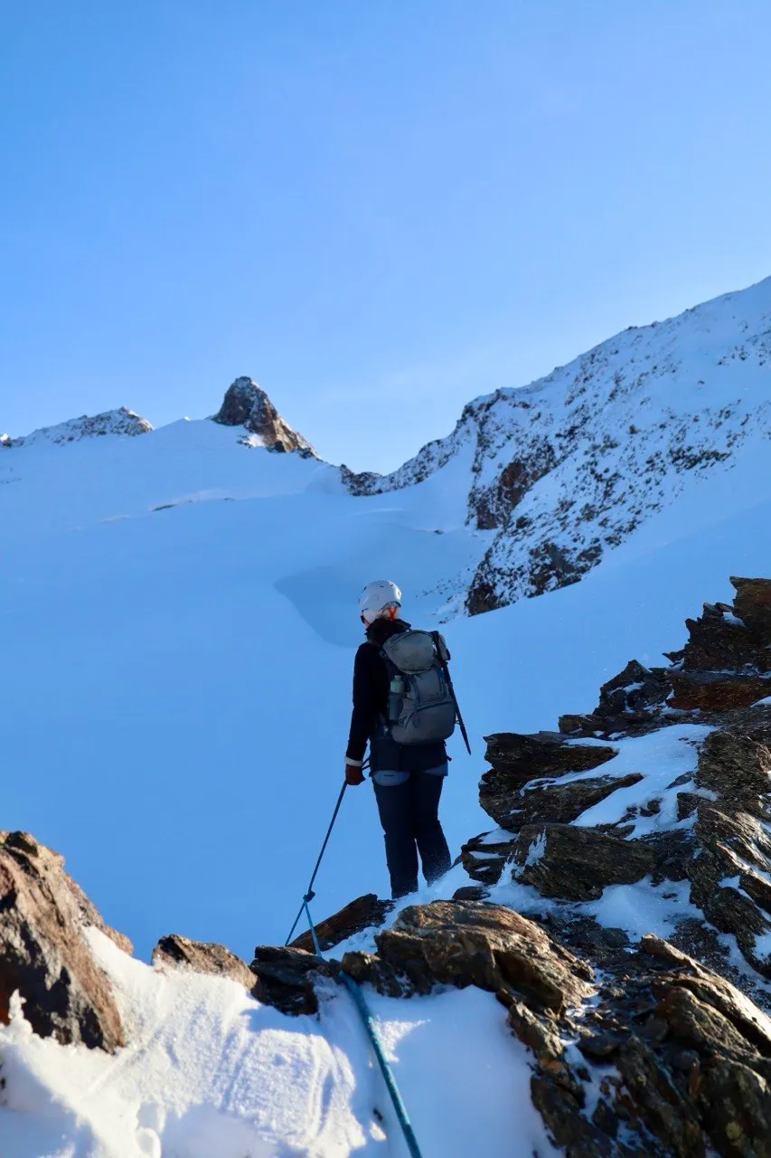 Hiker on a snowy ridge looking across toward a snow pinnacle.