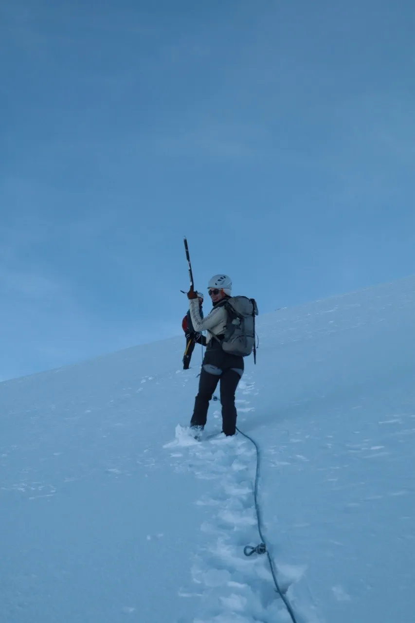 Hiker turning around on a steep snow slope, ice axe in hand.