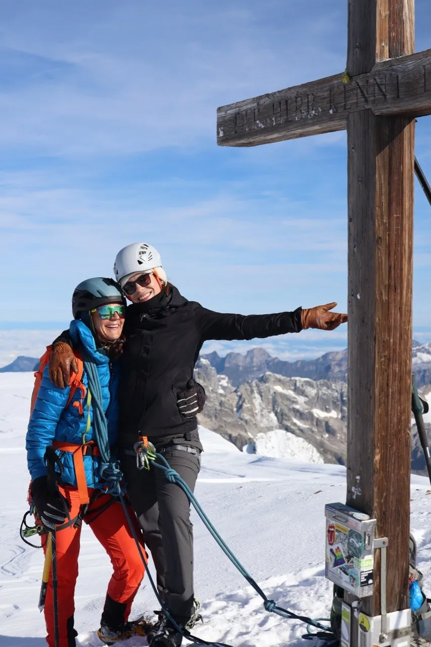 Two climbers embracing at the wooden summit cross of the Sustenhorn.