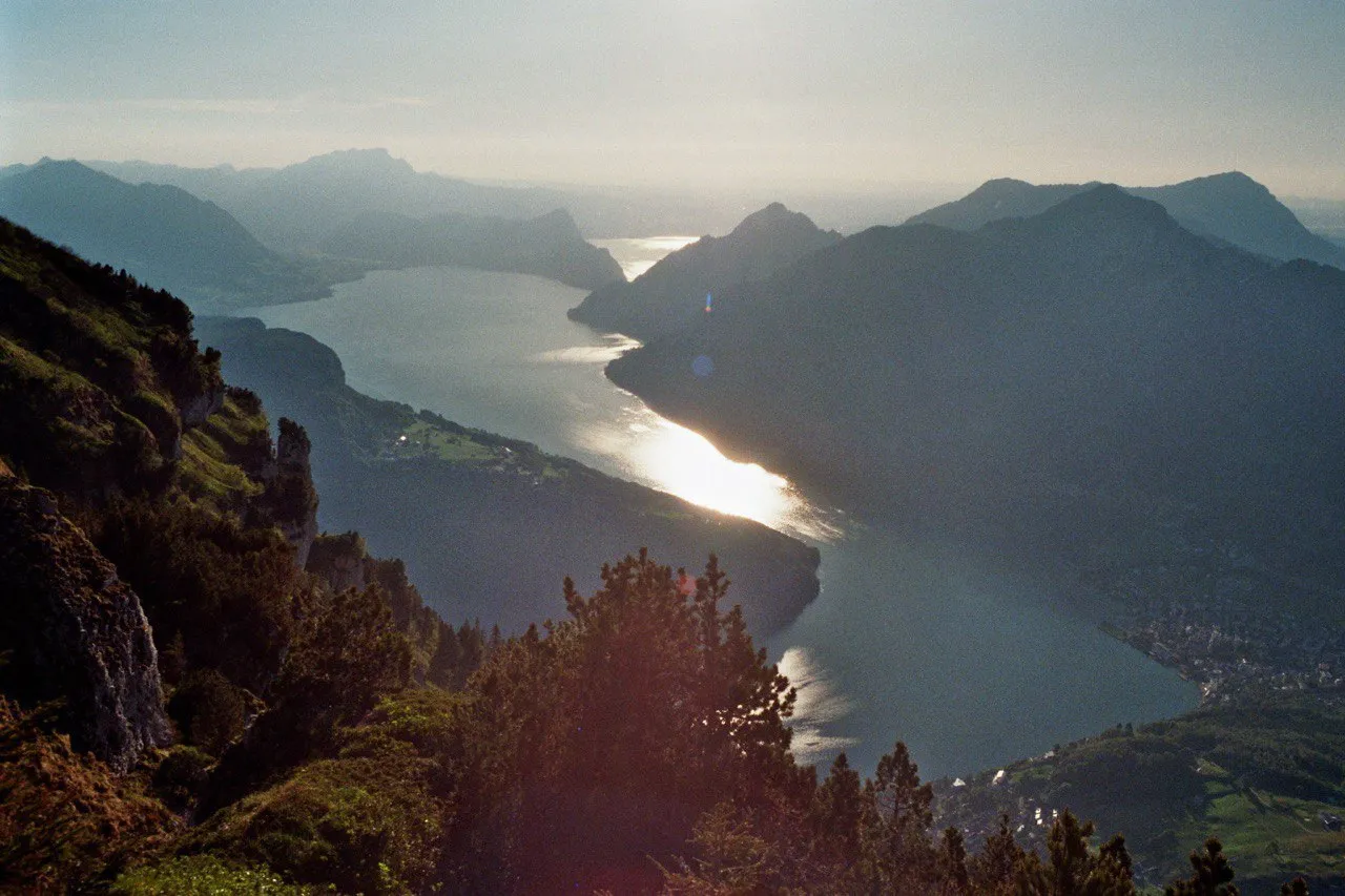 The Urnersee winds between dark mountain ranges in golden backlight, the water glittering under the low sun.
