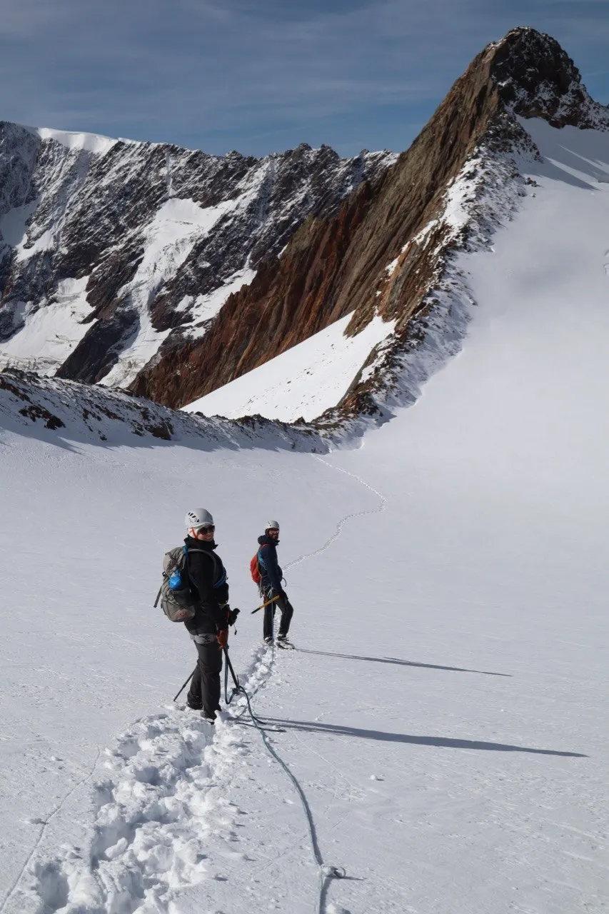 Two roped climbers on the glacier below a striking rock fin.