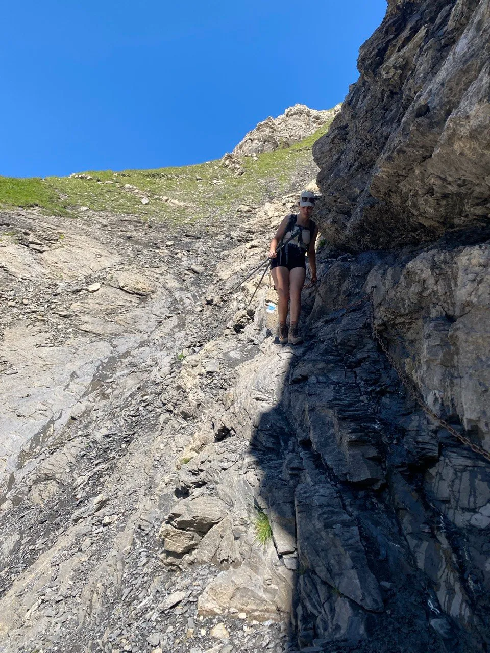 A hiker holds onto a chain along a steep, exposed rock section.