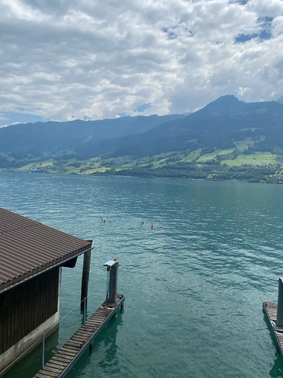 View from a boathouse over the turquoise Walensee, with several people swimming and mountains in the background.