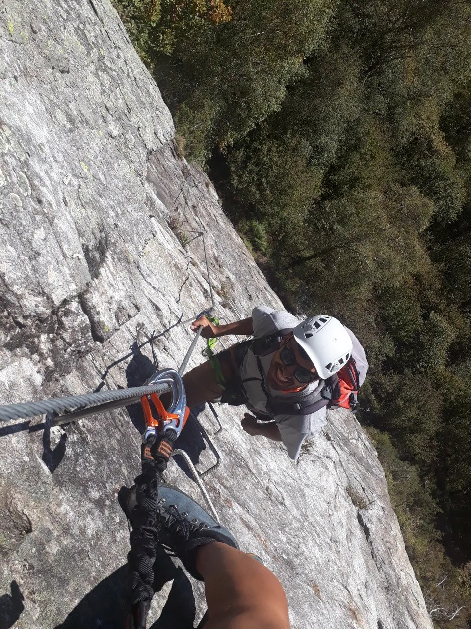Looking down at a grinning climber on a sunny granite slab, dense autumn forest below.