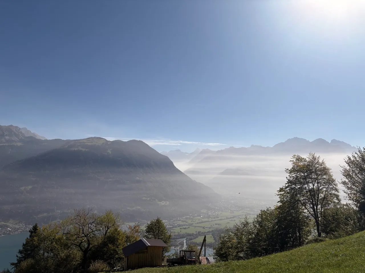 View from an alpine meadow with a small wooden hut over the mist-filled Reuss valley toward Lake Urnersee.