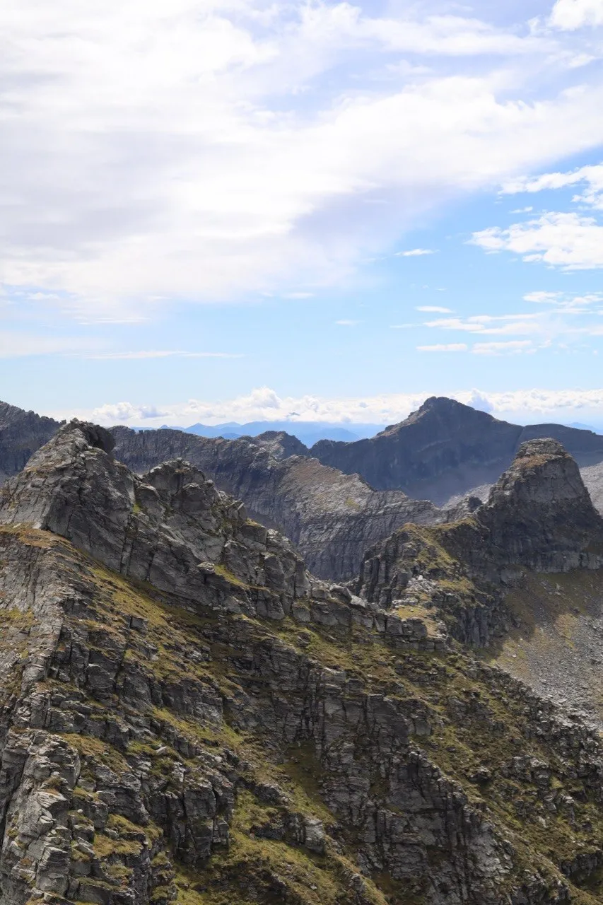 Jagged grey rock peaks and ridges under a bright, partly cloudy sky.