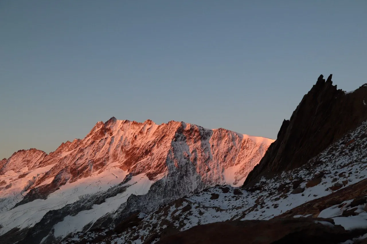 Alpenglow on the snowy Sustenhorn massif at dawn, with a sharp rock pinnacle on the right.