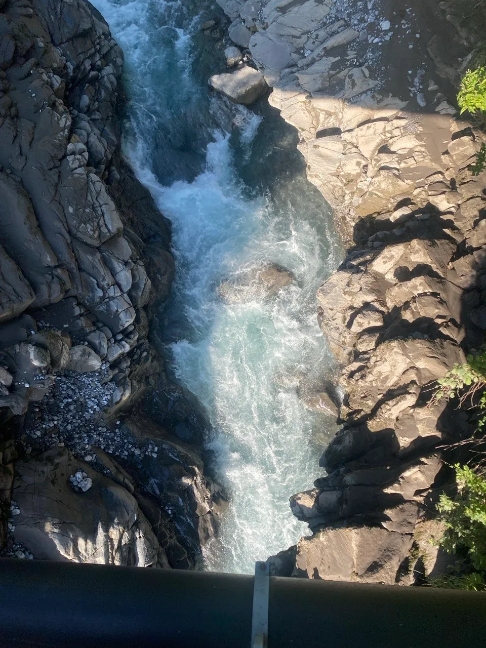 View from a bridge onto a roaring turquoise mountain stream squeezed through a narrow gorge.