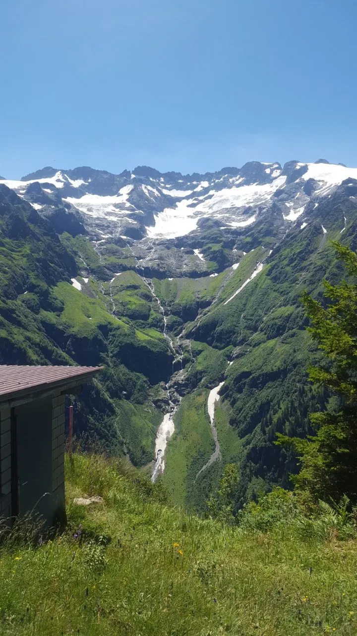 View from a hut across a deep green valley toward a glaciated mountain cirque laced with waterfalls.