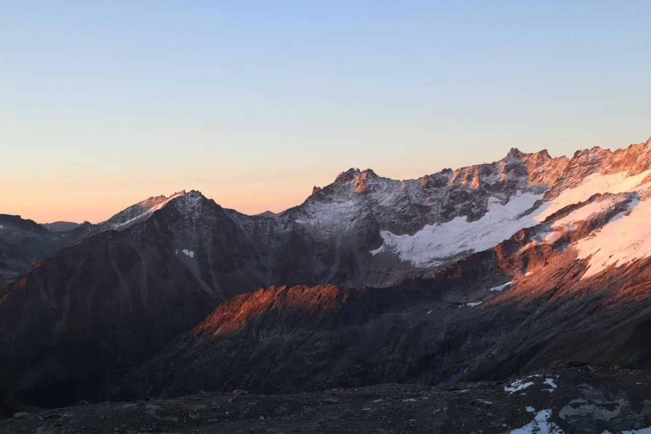 Mountain panorama at dawn with an orange glow on the horizon above dark ridges.