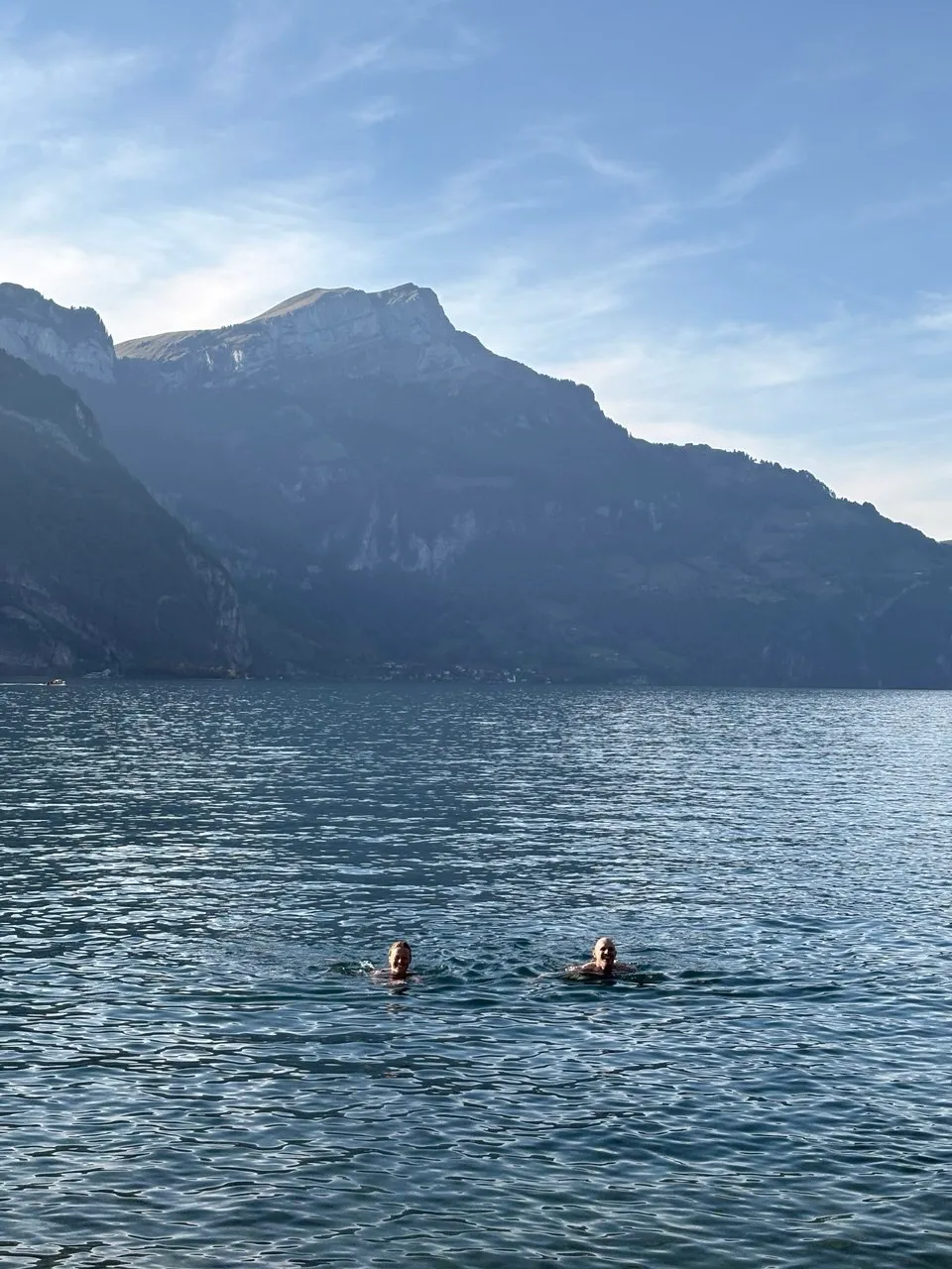 Two swimmers in the clear water of Lake Urnersee, with sheer cliffs dropping straight into the lake behind.